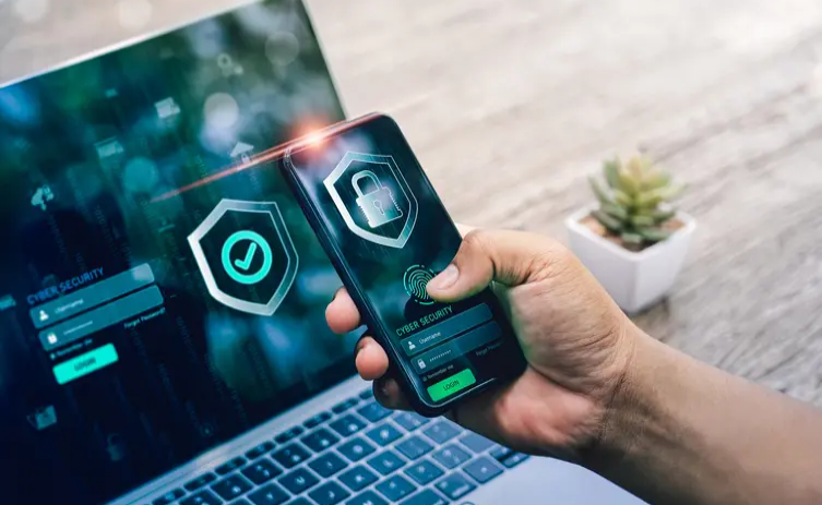 A person holding an iphone in front of a laptop.